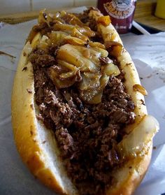 a close up of a hot dog on a bun with onions and meat in it