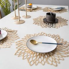 a white table topped with lots of plates covered in gold leafy designs and candles