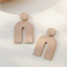 two pairs of pink earrings on top of a white surface with a wooden object in the background