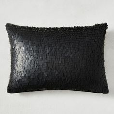 a black pillow with sequins on the front and back, against a white wall