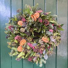 a wreath hanging on the side of a green door with pine cones and other flowers