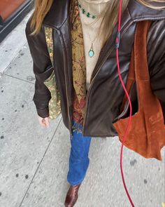 a woman walking down the street with her headphones in her ears and wearing a brown leather jacket