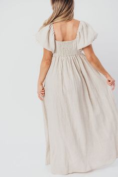 Join us in welcoming the *breathtaking* Candace Maxi Dress to the Worth Collective repertoire - we know you're going to love her! This neutral-hued, 100% linen dress is the epitome of elegance and luxury. Its beautiful neckline frames your decolletage, while the gently puffed sleeves and full skirt accent this gown's exquisite craftmanship. It's the perfect choice for this season's weddings, photo shoots, and other special events! FIT: Runs true to size. Empire waist and smocked bodice will accommodate early-to-mid maternity baby bumps. Long length (top of foot for our 5'7" models). MATERIAL: 100% Linen. GARMENT DETAILS: Short-sleeved maxi dress with an empire waist and full, flowing skirt. Features a square neckline, puffed sleeves that can be worn on or off the shoulder, and a structured Linen Maxi Dress With Smocked Back And Fitted Style, Fitted Linen Maxi Dress With Smocked Back, Linen Maxi Dress With Smocked Back, Chic Linen Maxi Dress With Smocked Back, Neutral Linen Midi Dress For Vacation, Flowy Beige Linen Dress, Beige Flowy Linen Dresses, Neutral Linen Dress With Relaxed Fit, Neutral Relaxed Linen Dress