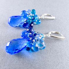 "Stunning cobalt blue lab created topaz dangle below a generous cluster of sparkling briolettes consisting of turquoise blue, navy blue, peacock green and sky blue quartz. I have used all sterling silver to keep them fresh. The gems are topped off with another blue topaz gem and a sterling silver bead. The blue topaz measure 20x11mm. The total earring length is 2 1/8\" (54mm.) from the top of the lever back ear wires." Blue Briolette Earrings For Wedding, Blue Cluster Sterling Silver Jewelry, Blue Gemstone Accented Drop Earrings, Blue Drop Earrings With Gemstone Accents, Blue Gemstone Cluster Earrings As Gift, Blue Gemstone Cluster Earrings For Gift, Blue Sapphire Cluster Earrings For Gift, Blue Briolette Gemstone Earrings, Blue Peacock