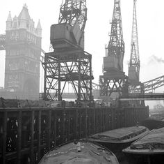 black and white photograph of boats docked at dock with cranes in the backgroud