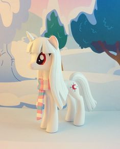 a toy pony with a scarf around it's neck standing in front of a wall