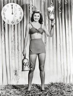 a woman in a bathing suit holding two boxing gloves and standing next to a clock