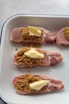 four pieces of meat with butter on them in a white dish, ready to be cooked