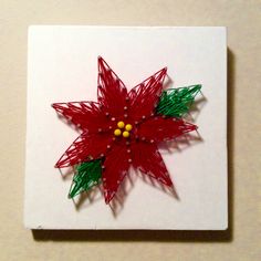 a red and green poinsettia is on a white square with yellow beads