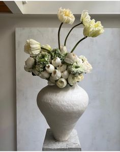 a white vase filled with flowers on top of a marble block in front of a wall