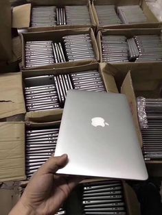 a person holding an apple laptop in front of many boxes with silver bars on them