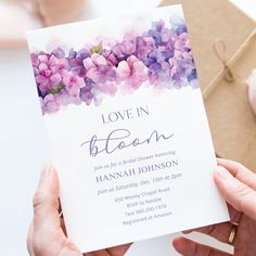 a woman holding up a card that says love in bloom with purple flowers on it