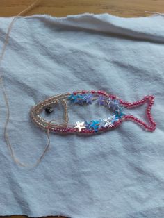 a fish made out of beads and string sitting on top of a piece of paper