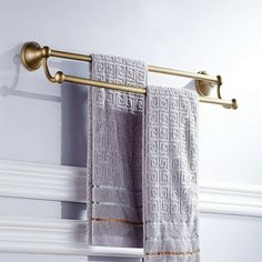 two towels hanging on a towel rack in front of a white wall with the words okaros above it