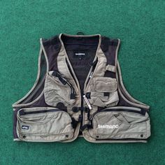 a vest with pockets and zippers sitting on the green carpet in front of a pair of scissors