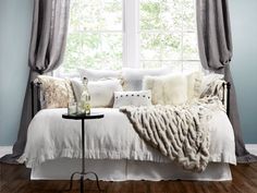 a bed with pillows and blankets on top of it in front of a large window