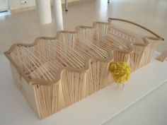 a sculpture made out of sticks and yarn with a yellow flower on the top of it