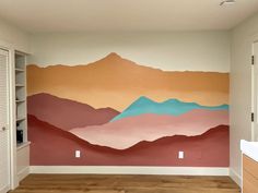 an empty room with painted mountains on the wall and wood flooring in front of it