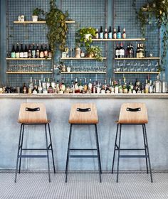 three wooden stools sitting in front of a bar with bottles on the back wall