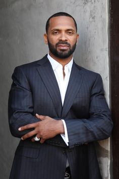 a man in a suit and tie leaning against a wall with his arms crossed looking at the camera