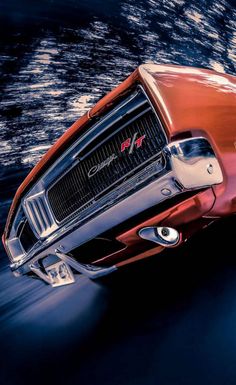 the front end of a red sports car driving on a road with water in the background