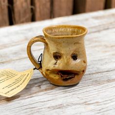 a ceramic coffee cup with a face drawn on it and a note attached to the handle