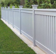 a white picket fence with green grass and trees in the backgroung area