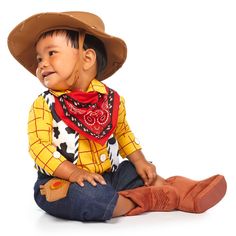 a little boy sitting on the ground wearing a cowboy hat and bandana with his hands in his pockets