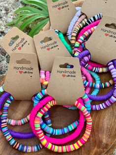 several colorful bracelets sitting on top of a wooden table next to a potted plant