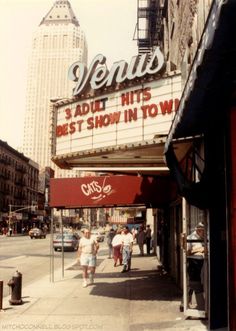 people walking on the sidewalk in front of a theater sign that reads venus, about hits best show in town