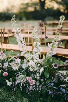 an arrangement of flowers and greenery in front of rows of wooden benches on the grass