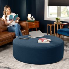 a woman sitting on a couch reading a book in her living room with a blue ottoman