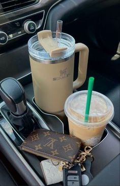 there are two drinks in the cup and a wallet on the car dash board with keys