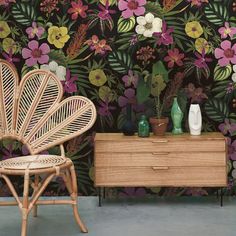 a wicker chair next to a wooden dresser and wallpaper with flowers on it