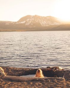 a woman is sitting in the sand by the water with her back to the camera