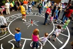 several children are standing in front of a chalk drawing on the ground while adults watch