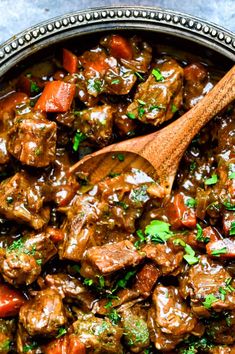 a pot filled with meat and carrots next to a wooden spoon on top of a table