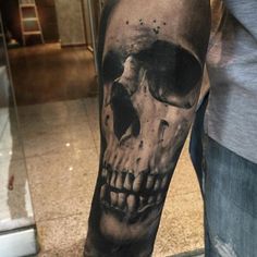 a man's arm with a black and grey skull tattoo on the left forearm