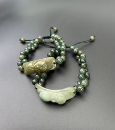 Introducing a pair of exquisite Green Genuine Jade Beaded Bracelets. Crafted with care and precision, these bracelets are adorned with authentic jade beads, showcasing a stunning array of green hues that radiate natural beauty. Each bracelet comes with the design of a traditional Chinese spirit animal (Pixiu), Pixiu is considered a powerful protectors of feng shui practitioners. The real green jade bead bracelets are adjustable and perfect for gifting. Some Highlights of the genuine dark & green Good Luck Adjustable Beaded Bracelets With Natural Stones, Traditional Adjustable Jade Bracelets, Traditional Adjustable Jade Bracelet, Adjustable Gemstone Beads Bracelets For Good Luck, Adjustable Carved Bracelets With Round Beads, Spiritual Carved Beaded Bracelets, Adjustable, Spiritual Carved Beaded Bracelets, Adjustable Carved Beaded Spiritual Bracelets, Adjustable Carved Bracelets