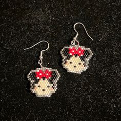 a pair of beaded earrings with a dog wearing a red bow on the ear