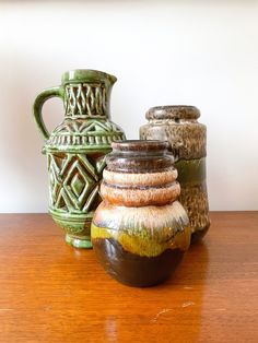 three vases sitting on top of a wooden table next to each other and one is green