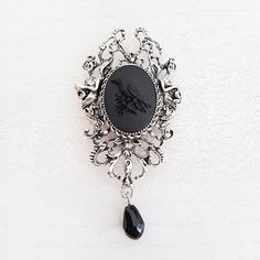 Antique silver Gothic style Victorian inspired large cameo 2 in 1 necklace brooch in black. The cameo is completely black, with detailed black raven, and is set in an ornate antique silver plated setting on a long antique silver plated chain. Underneath is a faceted black glass teardrop bead. The brooch can be easily threaded onto the chain to make a necklace. The setting is 3 inches (75 mm) from top to bottom, including the bead, and has a brooch fastening on the back, the matching chain has a Gothic Formal Jewelry Brooch, Gothic Brooch Jewelry Gift, Black Brooch Jewelry Gift, Black Brooch Jewelry As Gift, Black Brooch Jewelry For Gift, Black Gothic Jewelry Brooch, Black Gothic Brooch Jewelry, Black Gothic Brooch, Victorian Black Brooches As Gift