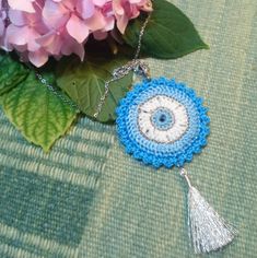 a blue and white crocheted evil eye pendant with tassels on a chain