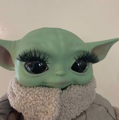 the baby yoda doll has long eyelashes and is wearing a white sweater with a black collar