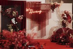 a red carpeted area with flowers and curtains on the wall that says wedding written in neon lights