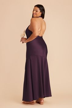 a woman in a long purple dress with her back turned to the camera and holding a flower