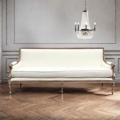 a white couch sitting next to a chandelier on top of a wooden floor