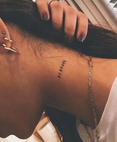 a woman with a small tattoo on her neck and behind her head is a gold chain