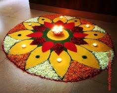 a lit candle is placed in the center of a flower arrangement on the floor with grass