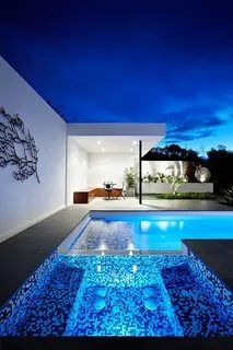 an outdoor swimming pool at night with blue lights on the walls and water running through it